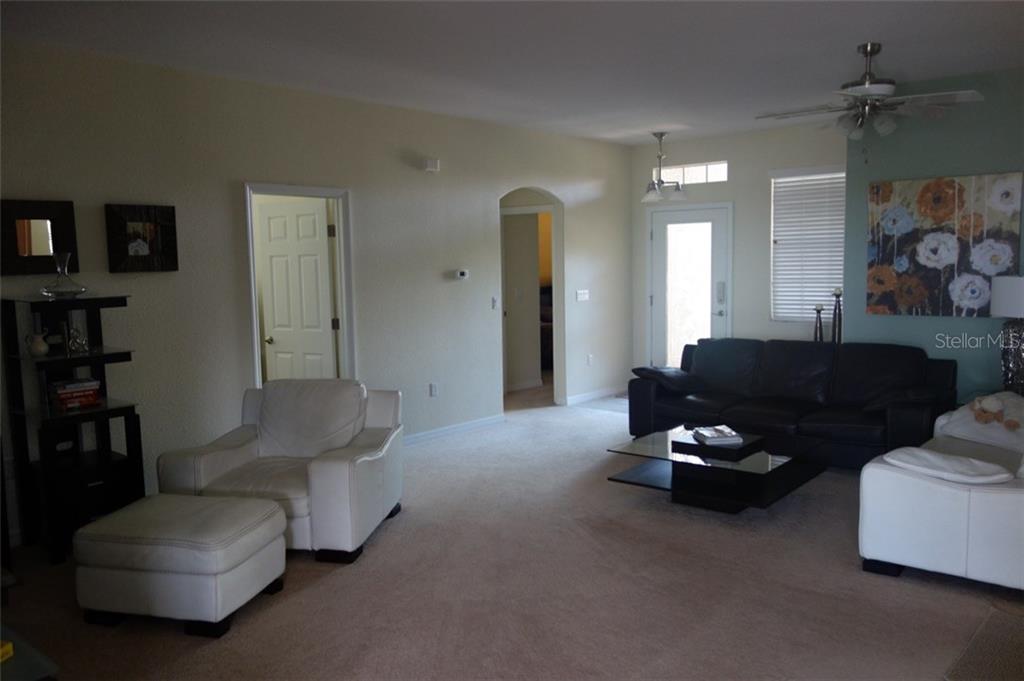 A living room features beige carpet, a white armchair with ottoman, and a dark sofa — 115 RIVER ENCLAVE CT. COURT, BRADENTON, FL
