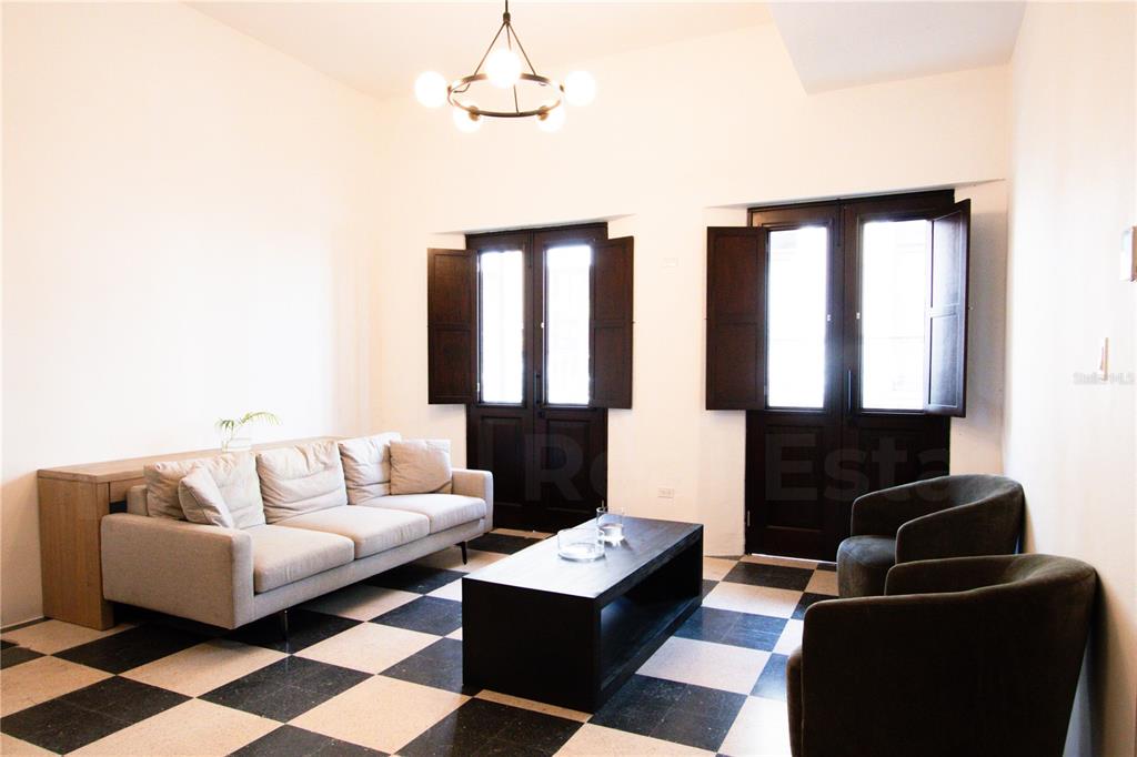 A living room features a checkered floor, a light-colored sofa, two dark armchairs, and shutters — 254-256 SAN FRANCISCO STREET UNIT 201, SAN JUAN, PR