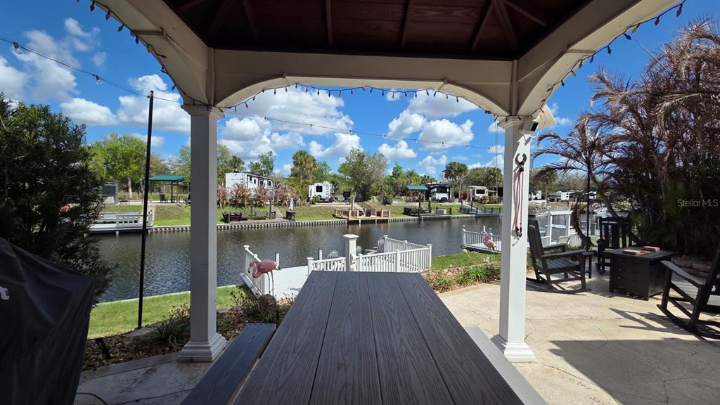 A covered patio overlooks a canal with a dock, lawn, and parked recreational vehicles — 431 WATERWAY DRIVE, RIVER RANCH, FL