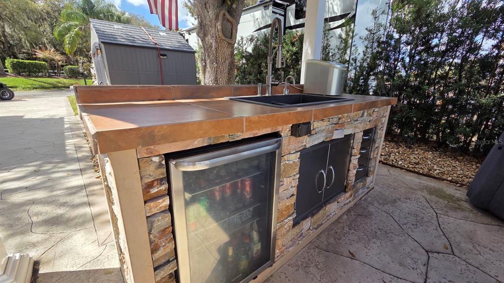 An outdoor kitchen features a stone base, tiled countertop, sink, and a built-in beverage refrigerator — 431 WATERWAY DRIVE, RIVER RANCH, FL