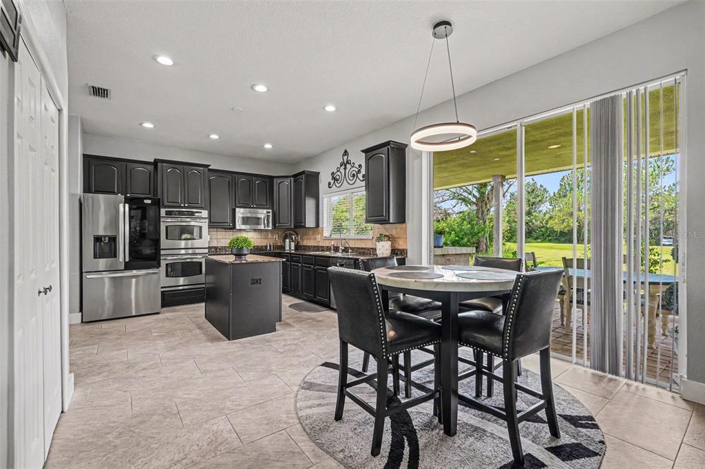 A kitchen with dark cabinets, stainless steel appliances, a center island, and granite countertops — 12915 CARLINGTON LN, RIVERVIEW, FL
