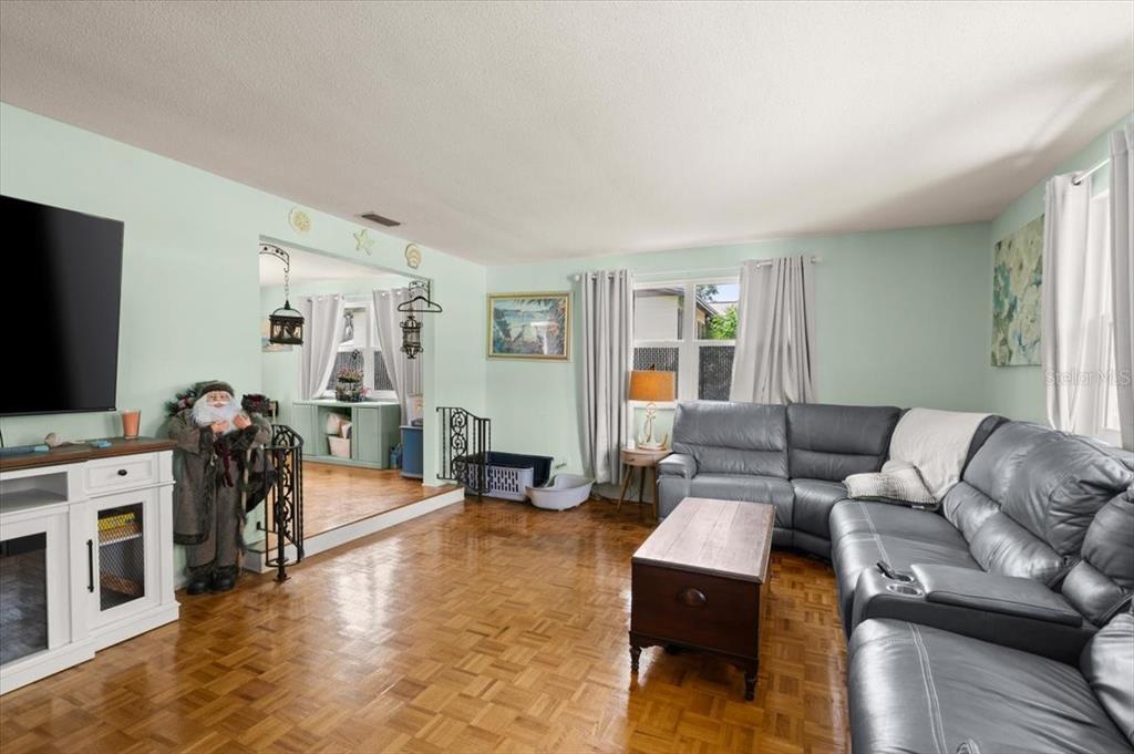 A living room with parquet wood flooring, a grey sectional sofa, and a white media console — 20 PUTNAM AVENUE, ORMOND BEACH, FL