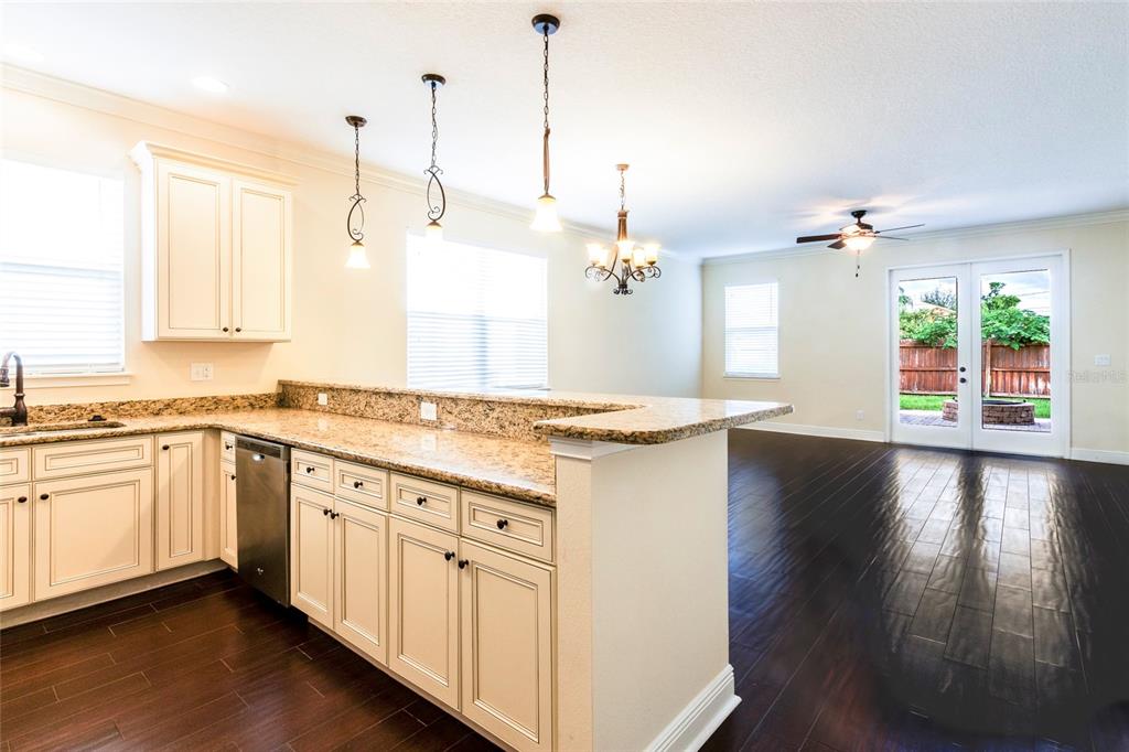 A kitchen with granite countertops and white cabinets overlooks a living area with dark floors — 1407 E MURIEL STREET, ORLANDO, FL