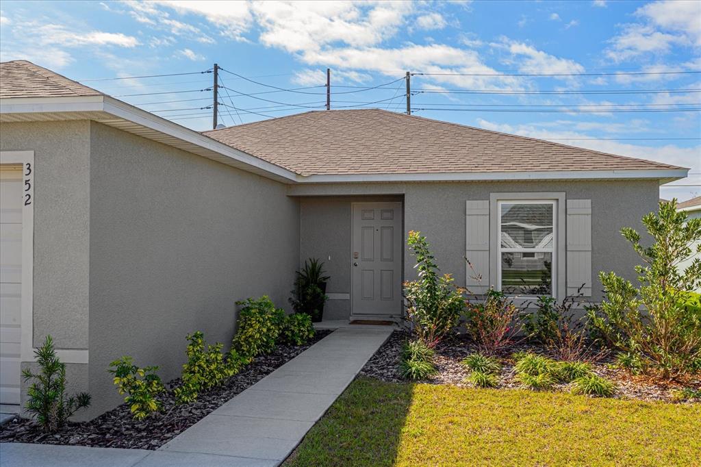 A single-story house exterior features a gray stucco facade, a walkway, and a front door — 352 TOWNS CIRCLE, HAINES CITY, FL