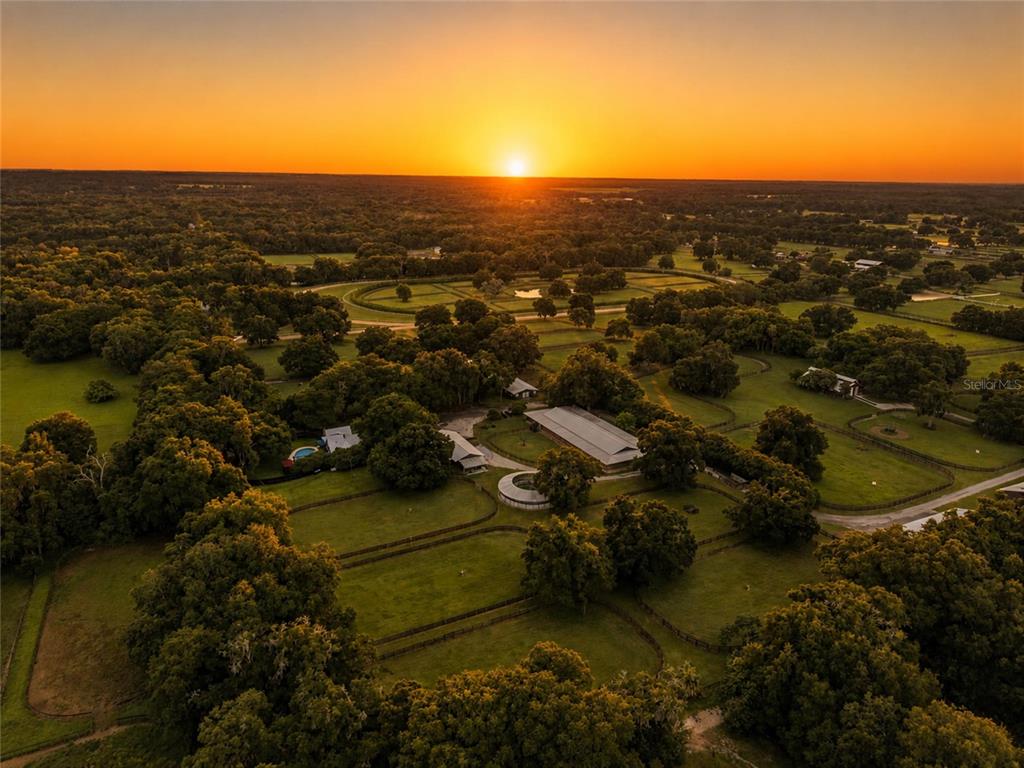 An aerial view shows a rural property with a large barn, pastures, and trees at sunset — 3825 NW 160TH STREET, REDDICK, FL