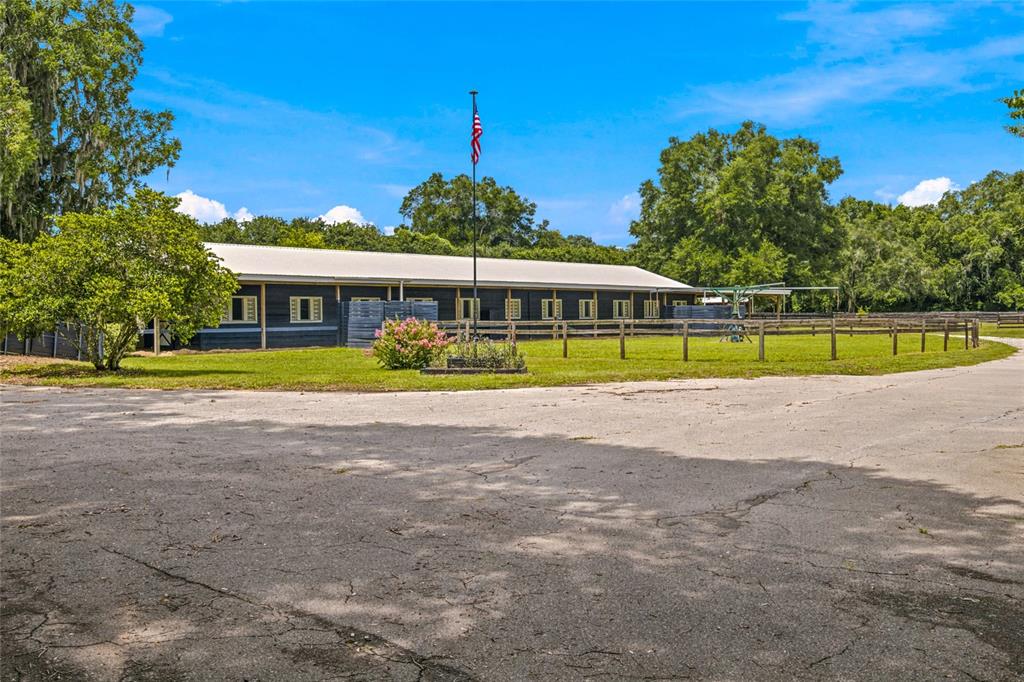 A long, dark-sided stable building sits behind a wooden fence on a grassy lot — 3825 NW 160TH STREET, REDDICK, FL
