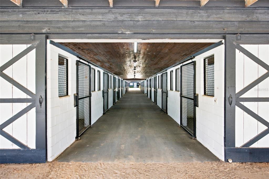 A long, central aisle of a horse stable features rows of stalls with metal grates — 3825 NW 160TH STREET, REDDICK, FL