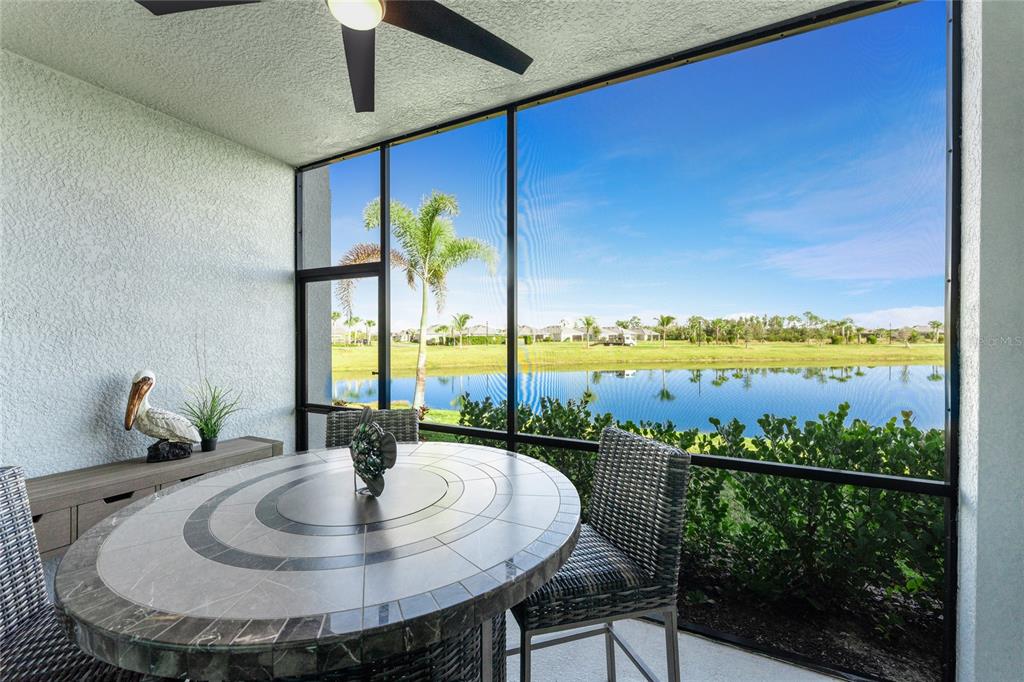 A screened-in patio features a tiled dining table, wicker chairs, and a view of a lake — 14267 HERITAGE LANDING BOULEVARD UNIT 1212, PUNTA GORDA, FL