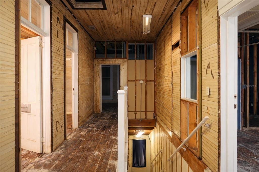 An interior hallway under renovation features exposed wood lath walls, wood flooring, and a staircase — 528 12TH STREET W, BRADENTON, FL