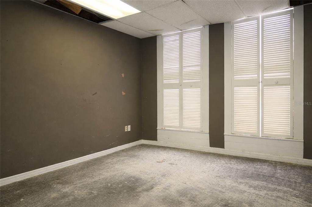 An empty room features dark gray walls, gray carpeting, a drop ceiling, and shuttered windows — 528 12TH STREET W, BRADENTON, FL