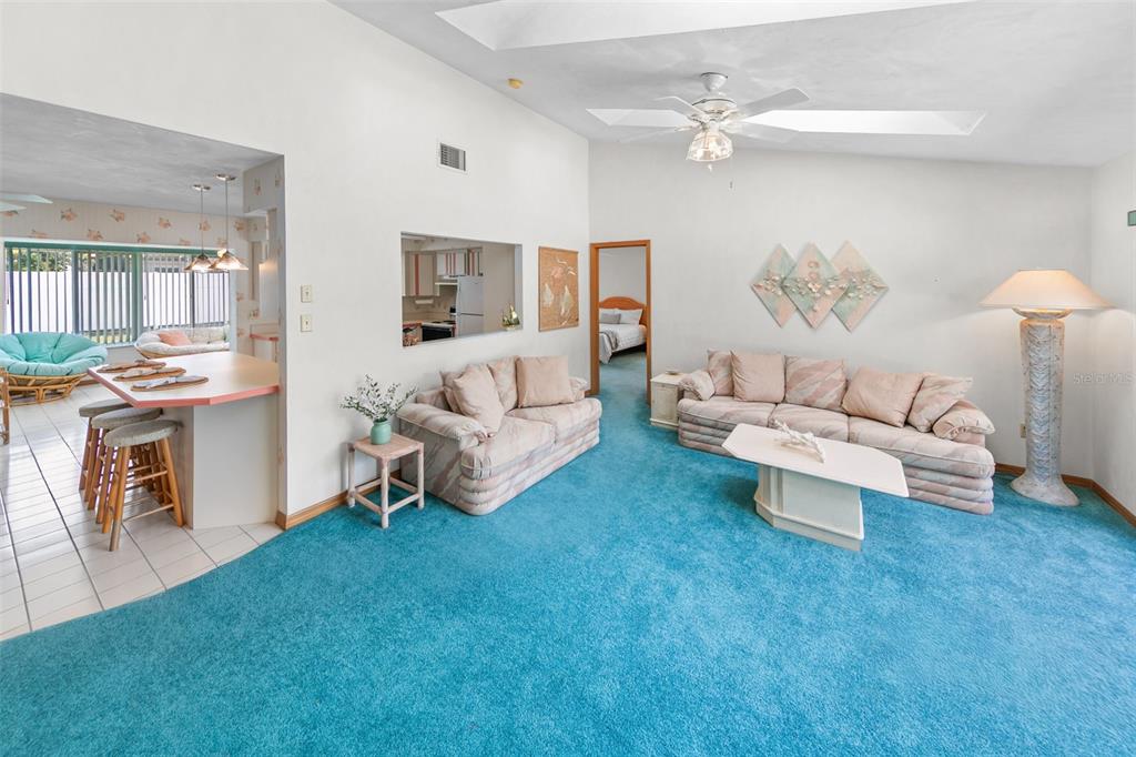 A living room with blue carpeting, two beige sofas, and a kitchen pass-through window — 4715 S PENINSULA DRIVE, PONCE INLET, FL