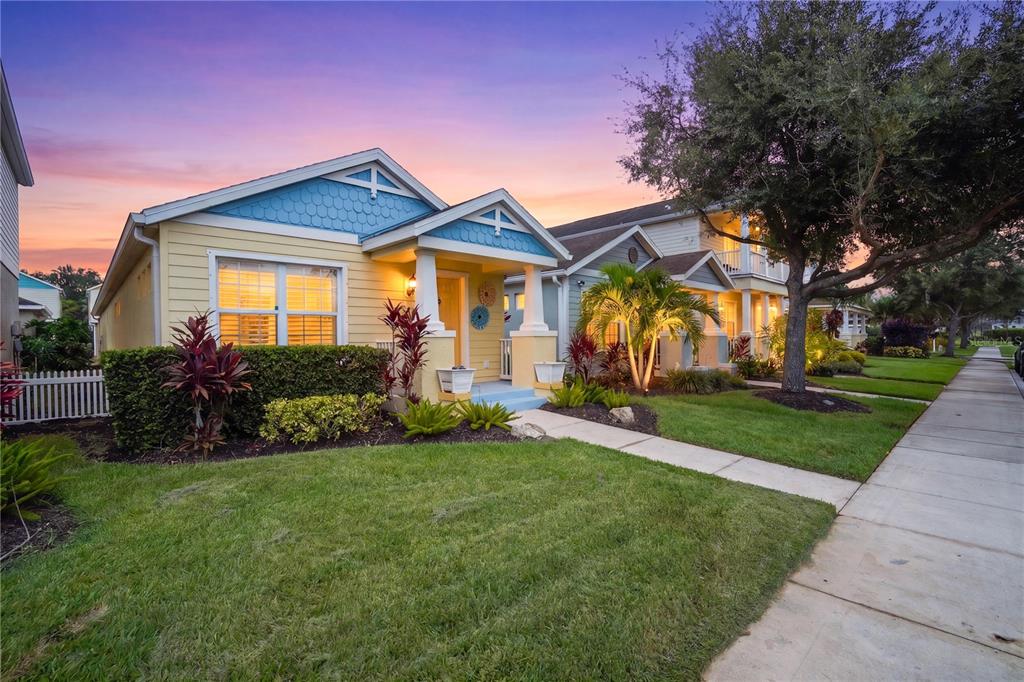 A yellow and blue house with a front porch sits next to a sidewalk at sunset — 4718 FOREST CREEK TRAIL, PARRISH, FL