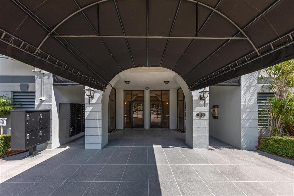A covered entryway features a black metal awning, glass double doors, and a tiled floor — 14820 RUE DE BAYONNE UNIT 505, CLEARWATER, FL