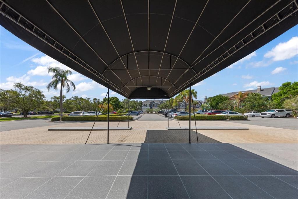 A large black metal canopy covers a paved driveway entrance in front of a parking lot — 14820 RUE DE BAYONNE UNIT 505, CLEARWATER, FL