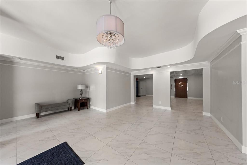 A spacious lobby features white marble-look tile flooring, a drum chandelier, and a gray bench — 14820 RUE DE BAYONNE UNIT 505, CLEARWATER, FL