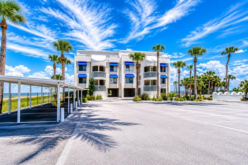 A multi-story white apartment building with blue awnings stands behind a parking lot and carport — 6504 SURFSIDE BOULEVARD UNIT 8, APOLLO BEACH, FL