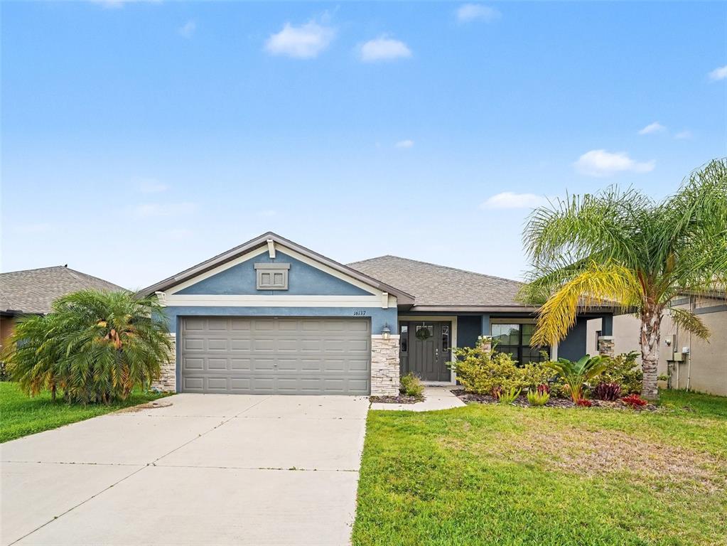A single-story house with a blue exterior, stone accents, a two-car garage, and palm trees — 16137 61ST LANE E, PARRISH, FL