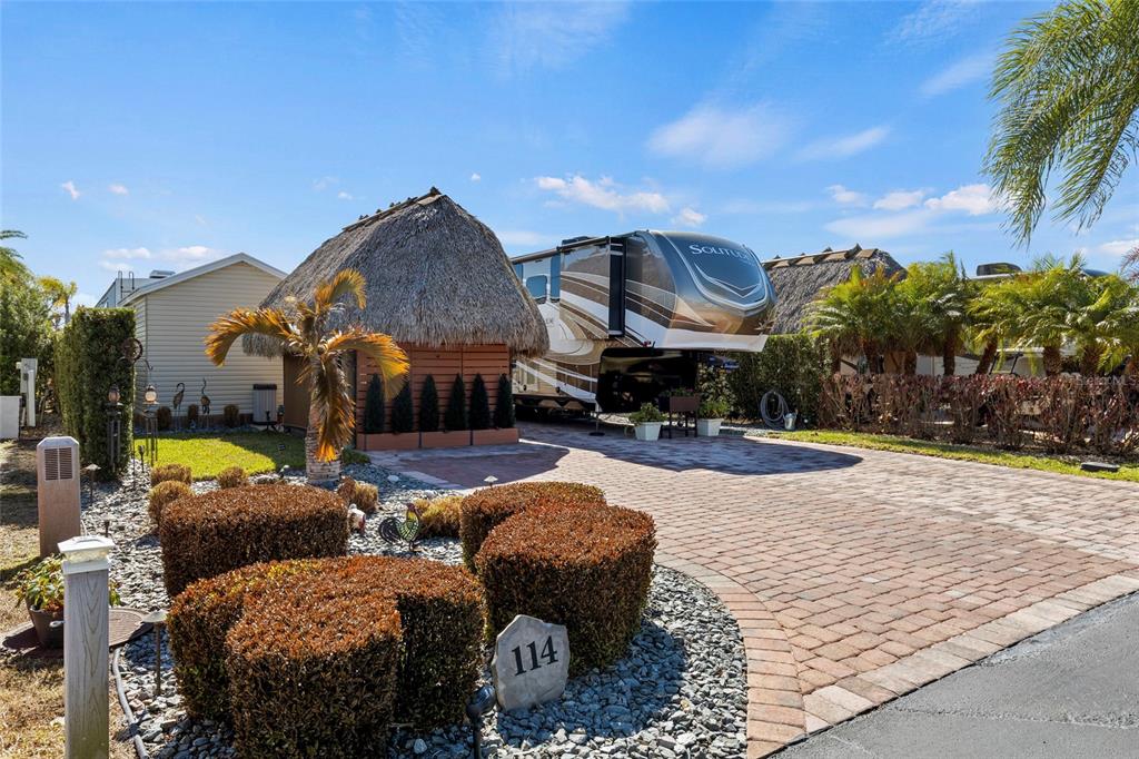 A paved driveway features a thatched-roof structure and a large recreational vehicle at lot 114 — 532 SW 38TH TRACE, OKEECHOBEE, FL