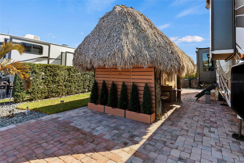 A thatched-roof tiki hut sits on a brick patio next to a parked recreational vehicle — 532 SW 38TH TRACE, OKEECHOBEE, FL