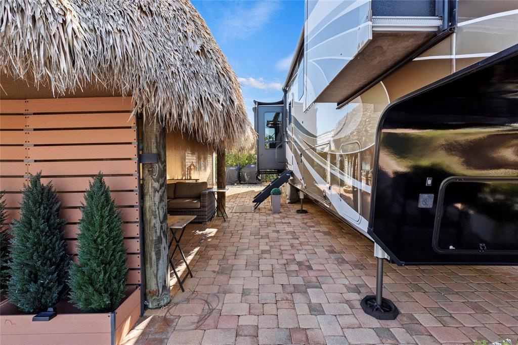 A paved patio area features a thatched-roof tiki hut beside a large parked recreational vehicle — 532 SW 38TH TRACE, OKEECHOBEE, FL