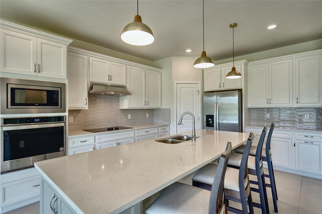 A modern kitchen features white cabinetry, stainless steel appliances, a quartz island, and pendant lighting — 6030 ARBOR WATCH LOOP, ORLANDO, FL