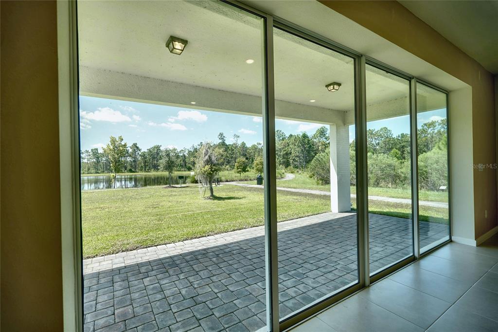 A view from inside a room through large sliding glass doors onto a paved patio — 6030 ARBOR WATCH LOOP, ORLANDO, FL
