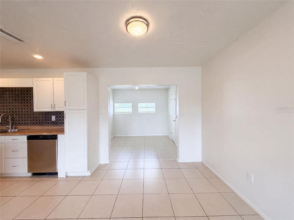 A kitchen with white cabinets and stainless steel appliances opens into a tiled dining area — 124 SAN BENITO AVENUE, NORTH PORT, FL