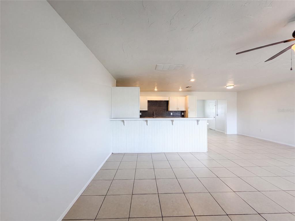 A kitchen with white cabinets and a breakfast bar overlooks a tiled living area — 124 SAN BENITO AVENUE, NORTH PORT, FL