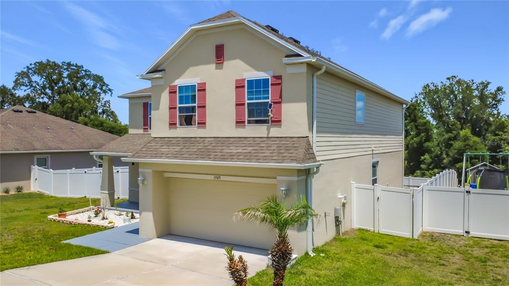 A two-story suburban house with a beige stucco exterior, a two-car garage, and red shutters — 15523 GEMINI DRIVE, MASCOTTE, FL