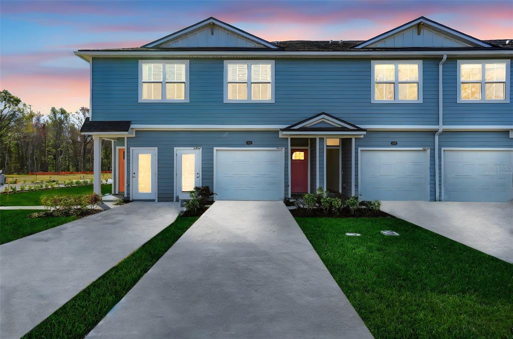 A two-story blue townhouse with two garage doors and a concrete driveway at sunset — 9174 TENDER LANE, JACKSONVILLE, FL