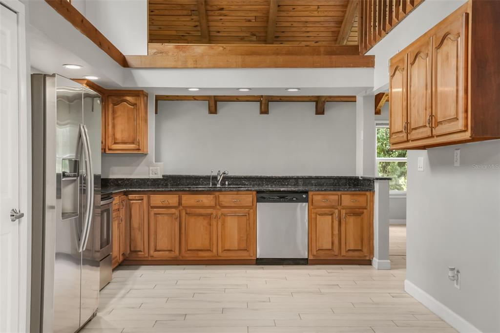 A kitchen features wood cabinets, dark granite countertops, stainless steel appliances, and a vaulted ceiling — 280 HUNTERS POINT TRAIL, LONGWOOD, FL