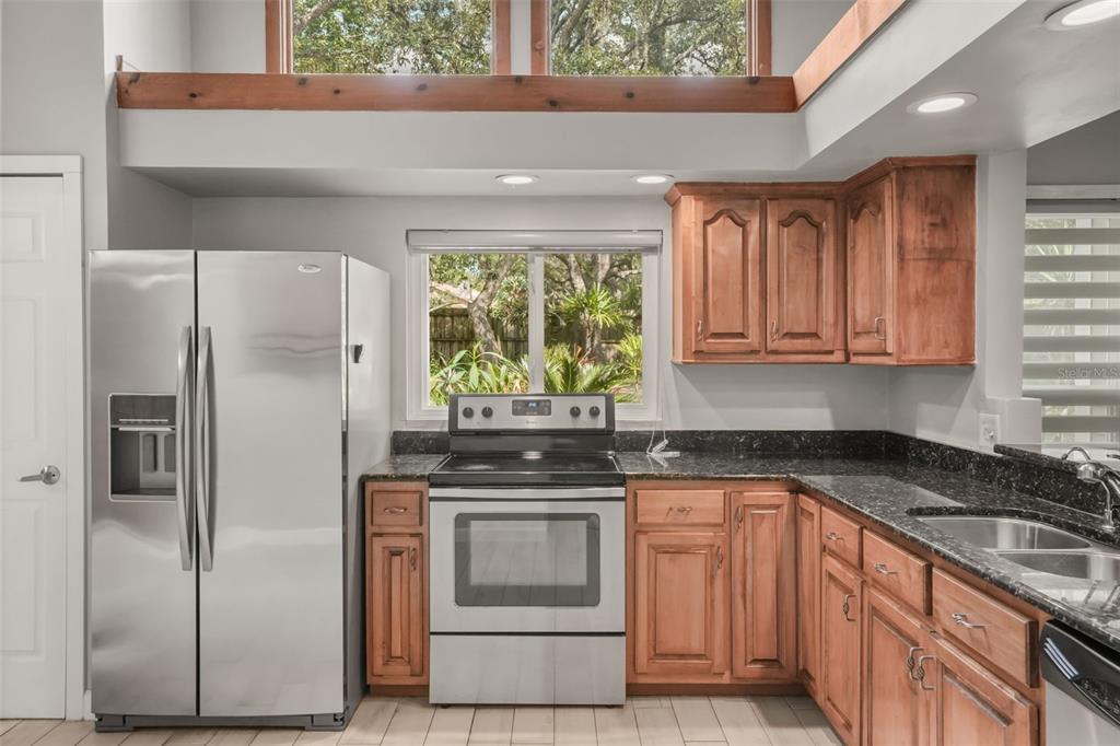 A kitchen features stainless steel appliances, wood cabinets, and dark countertops under a high window — 280 HUNTERS POINT TRAIL, LONGWOOD, FL
