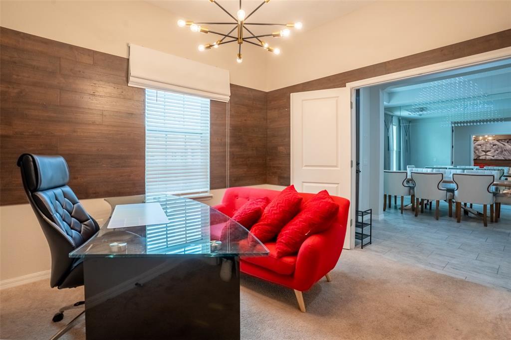 A home office features a glass desk, black chair, red sofa, and wood-paneled walls — 8304 LOOKOUT POINTE DRIVE, WINDERMERE, FL