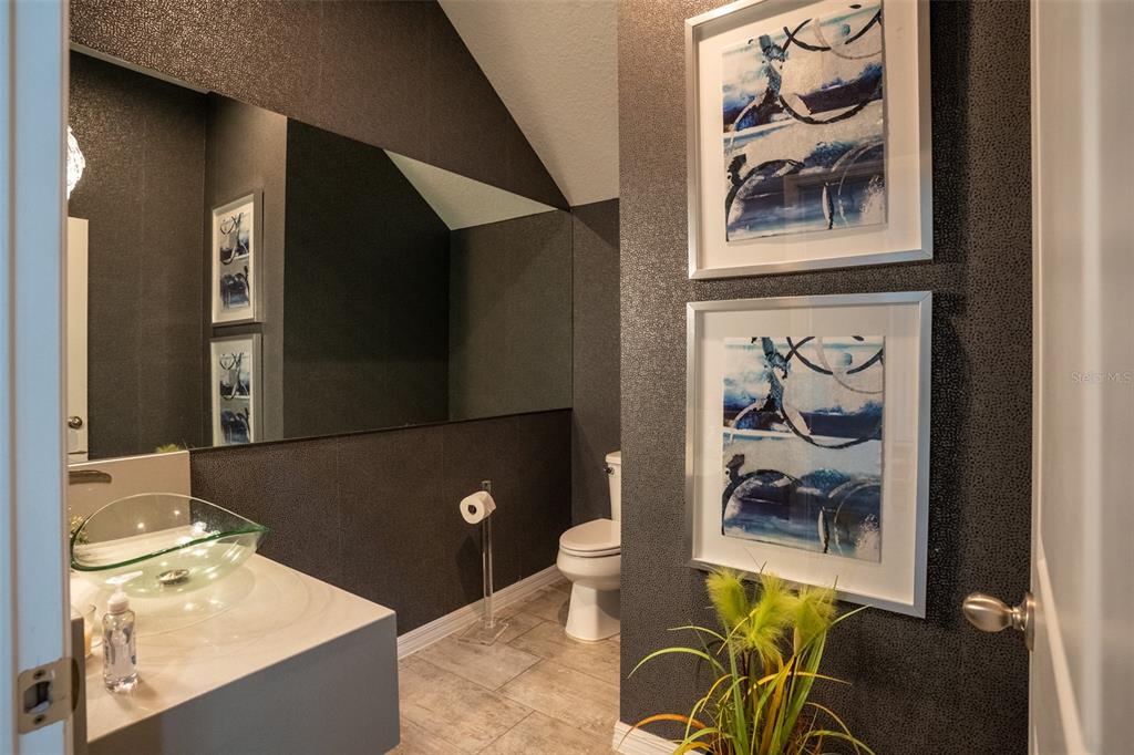 A powder room features dark textured wallpaper, a glass vessel sink, and two framed abstract prints — 8304 LOOKOUT POINTE DRIVE, WINDERMERE, FL