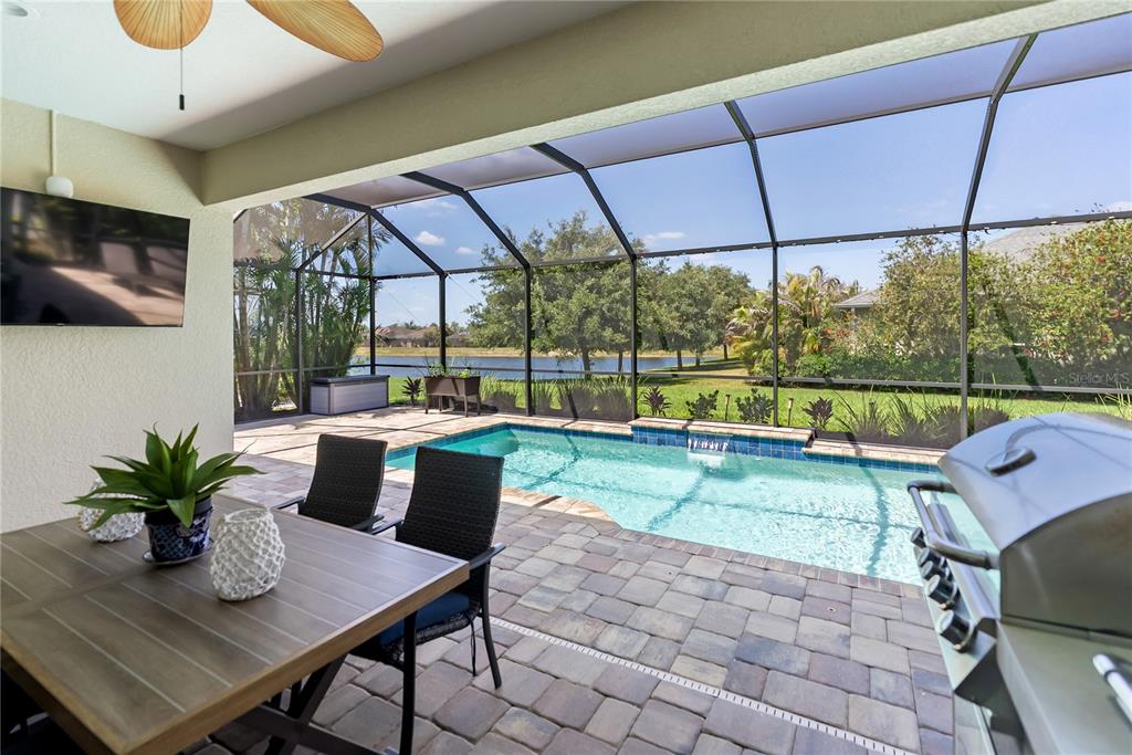 A covered patio features a dining set, a grill, and a screened-in pool overlooking water — 1215 THORNBURY DRIVE, PARRISH, FL