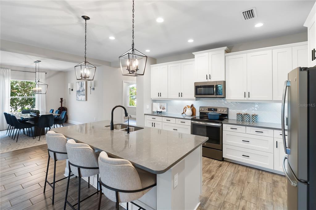 A kitchen features white cabinets, a gray island with bar seating, and wood-look tile flooring — 1215 THORNBURY DRIVE, PARRISH, FL