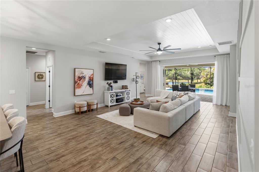 A bright living room features a large sectional sofa, a television, and sliding doors to a pool — 1215 THORNBURY DRIVE, PARRISH, FL