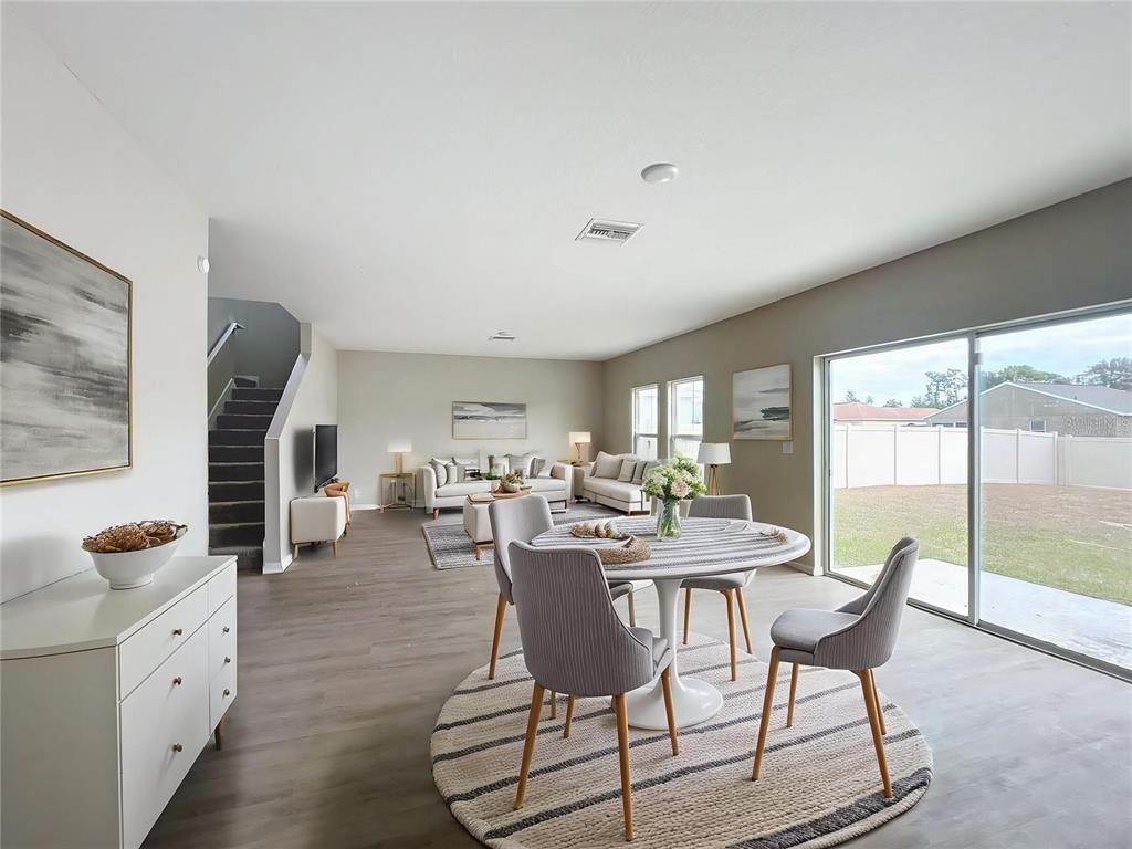 An open-concept living and dining area features light wood flooring, neutral walls, and sliding doors — 1404 AXEL CIRCLE, WINTER HAVEN, FL