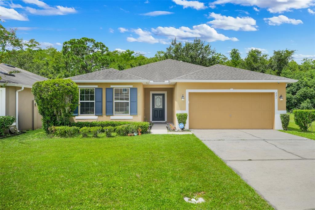 A single-story tan house with blue shutters, a two-car garage, and a front lawn — 221 DAIGLEDOG STREET, ST CLOUD, FL