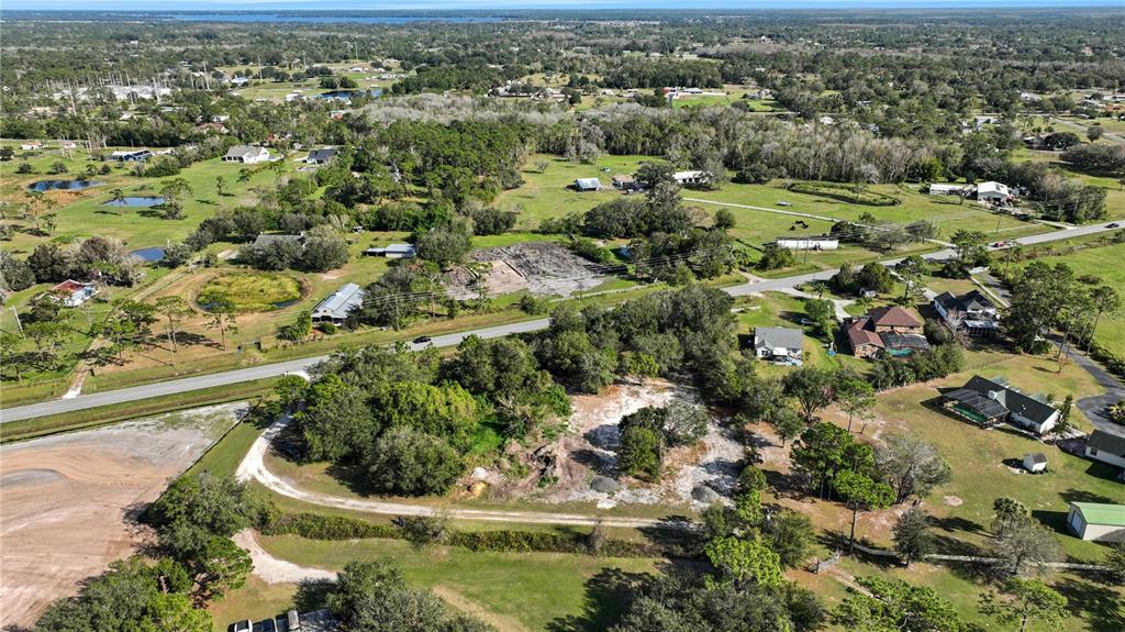 An aerial view shows a cleared, grassy lot surrounded by trees and nearby residential houses — CANOE CREEK ROAD, ST CLOUD, FL