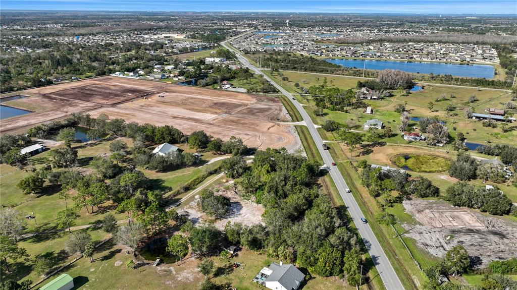 An aerial view shows a rural road separating a cleared construction site from residential properties — CANOE CREEK ROAD, ST CLOUD, FL
