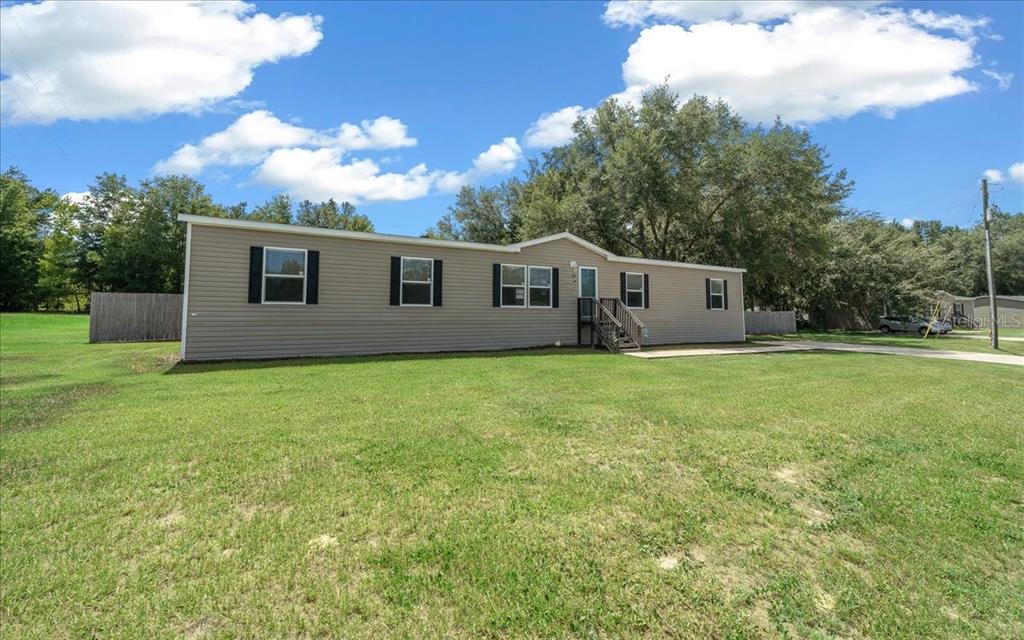 A single-story manufactured home with tan siding sits on a large, grassy lot — 38 SE 70TH CIRCLE, OCALA, FL