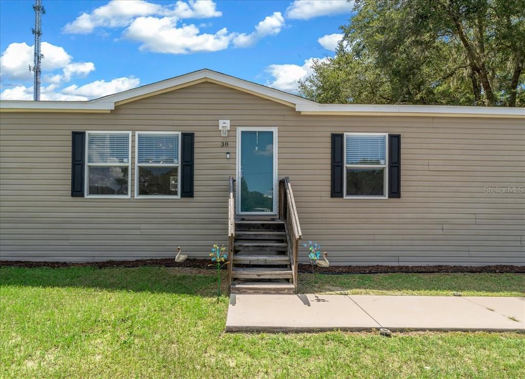 The exterior of a single-story manufactured home features tan siding, black shutters, and wooden stairs — 38 SE 70TH CIRCLE, OCALA, FL