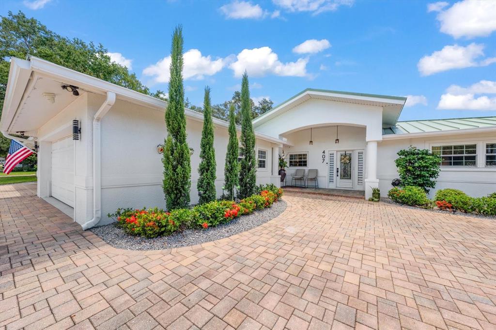 A white house with a paved driveway, three tall cypress trees, and an American flag — 407 HARBOR VIEW LANE, LARGO, FL