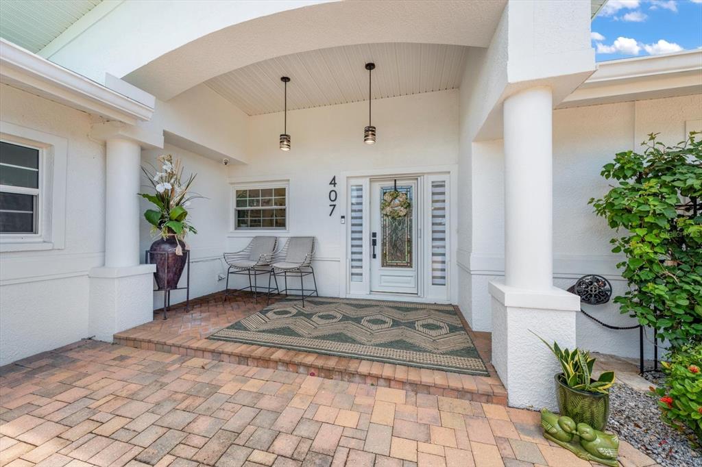 A covered entryway features a brick patio, two chairs, a patterned rug, and a front door — 407 HARBOR VIEW LANE, LARGO, FL