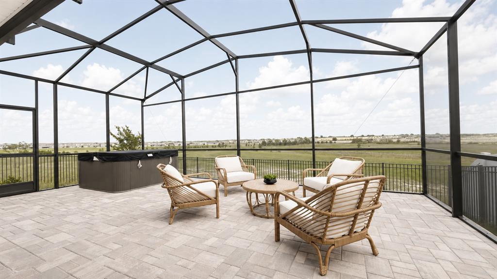 A screened-in patio features a hot tub, wicker furniture, and a view of a field — 3052 NAMASTE DRIVE, CLERMONT, FL