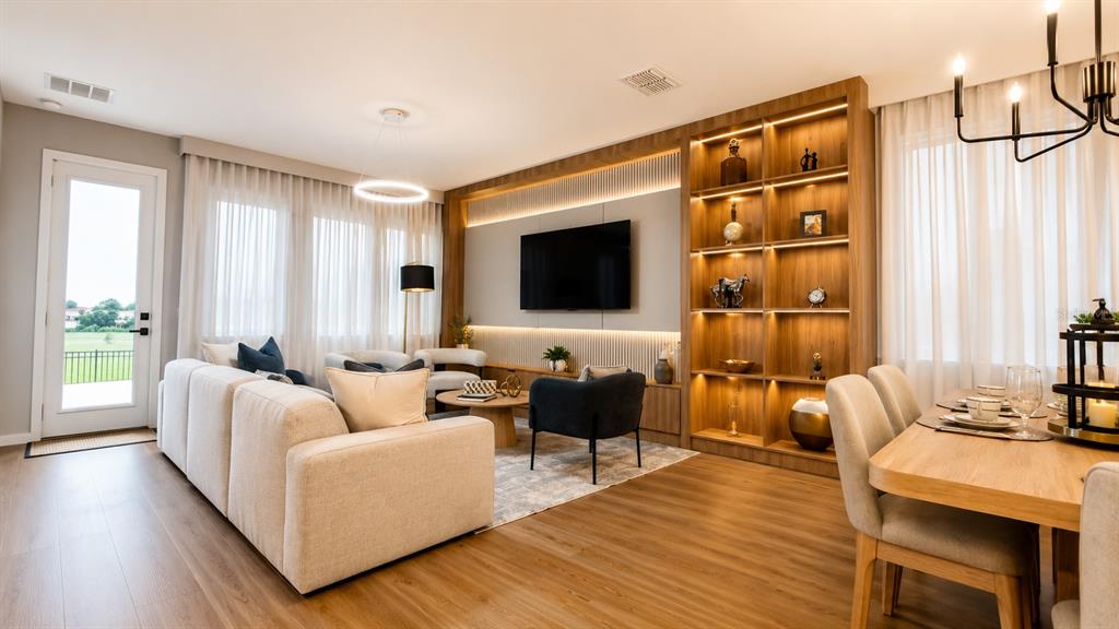 A modern living and dining area features wood flooring, a built-in bookshelf, and a television — 3052 NAMASTE DRIVE, CLERMONT, FL