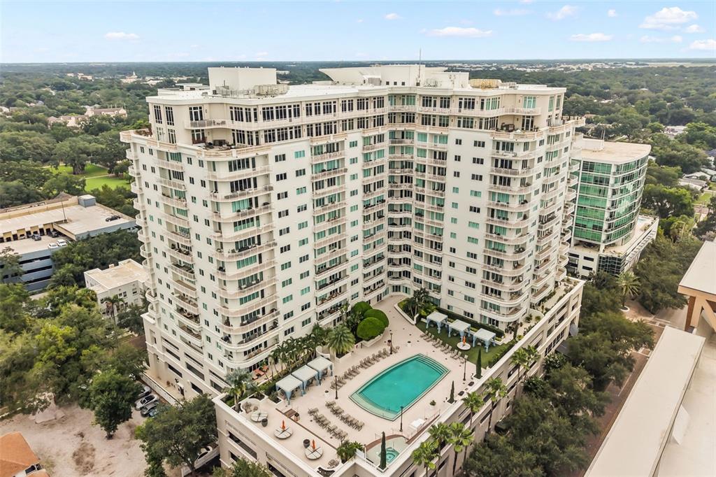An aerial view shows a large white apartment building with a swimming pool and courtyard — 100 S EOLA DRIVE UNIT 119, ORLANDO, FL