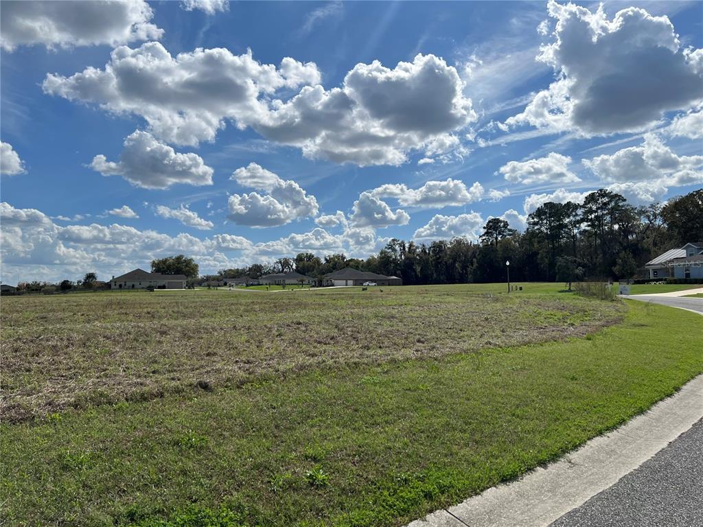 A vacant, grassy lot sits under a bright blue sky with scattered clouds — 000 NW 79TH LOOP Lot 14, OCALA, FL