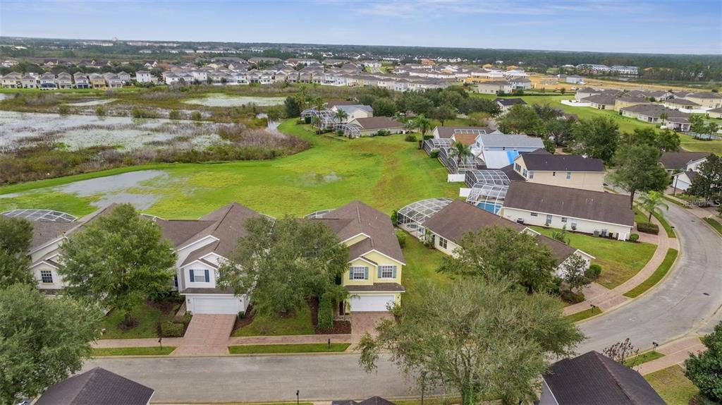 An aerial view shows suburban houses with swimming pools near a large grassy wetland area — 318 WINDSOR PLACE, DAVENPORT, FL
